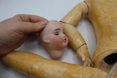 une main tenant une tête de poupée au-dessus d'un mannequin en bois