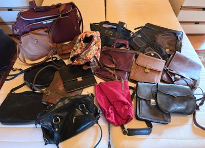 many different purses on a bed with a person standing next to them