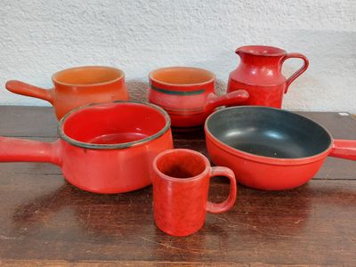 Plusieurs casseroles et poêles rouges sont posées sur une table en bois