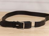 un gros plan d'une ceinture en cuir noir posée sur une table en bois