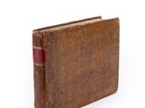 an old book with a red cover sitting on top of a white surface