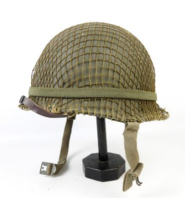 Un vieux casque est posé sur un support, sur une surface blanche.