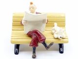 a figurine of a man sitting on a bench reading a newspaper