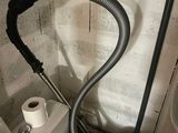 a toilet with a hose attached to it next to a toilet paper dispenser and a roll of toilet paper