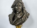 un buste en bronze représentant un homme coiffé d'un chapeau, posé sur un socle