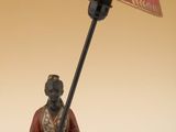 une statue représentant un homme assis sur un tabouret sur lequel est posée une lampe