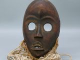 un vieux masque en bois entouré d'une corde, posé sur une surface grise