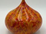 un vase rouge et jaune posé sur une surface blanche
