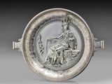 une image représentant une assiette en argent sur laquelle figure une femme assise à cheval