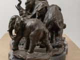statue of a herd of elephants walking across a wooden surface