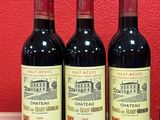 three bottles of red wine sit on a table in front of a red wall