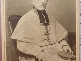 an old photo of a man in a priest ' s robes sitting in a chair