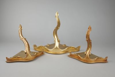 trois bougeoirs plaqués or posés sur des socles, sur une surface grise