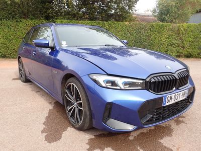 Une berline BMW Série 3 garée dans un parking, avec des buissons en arrière-plan