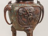 a bronze vase on a wooden stand with a bird on it