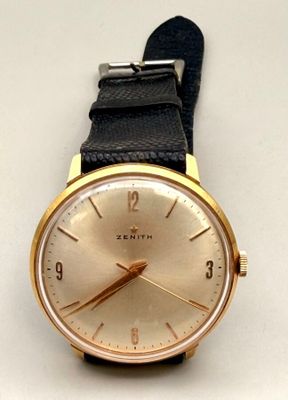 une montre en or avec un bracelet noir sur un fond blanc