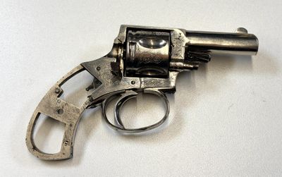 un revolver argenté posé sur une surface blanche, avec une crosse noire