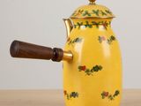a yellow tea pot with a wooden handle on a table