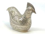 une figurine de poulet en argent posée sur une surface blanche