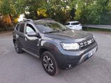 the grey dacia is parked in a parking lot near some trees