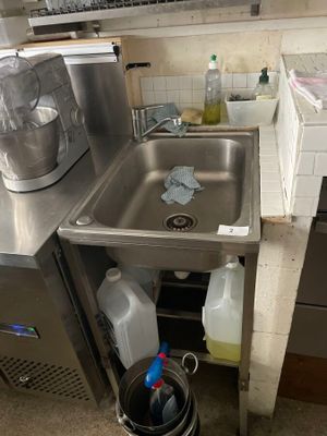 a sink in the corner of a kitchen next to a trash can