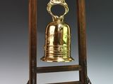 une cloche ancienne en laiton posée sur un socle en bois surmonté d'une couronne