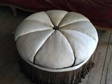 a round ottoman with fringes on it in a living room
