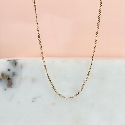 un collier à chaîne en or posé sur une dalle de marbre
