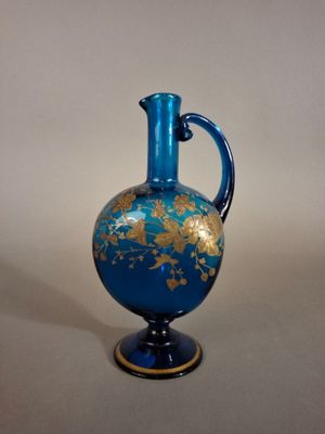 a blue and gold vase with a handle on a table