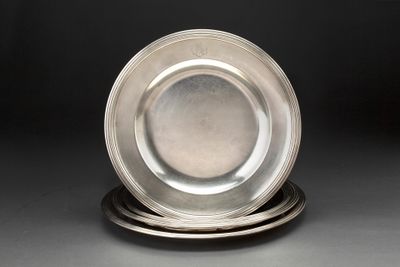 une assiette en argent posée au sommet d'une pile d'assiettes en argent