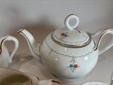 a white tea pot with a gold rim and a tea cup with a saucer on it