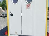 des toilettes portables blanches et jaunes installées sur un terrain recouvert de gravier