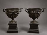 pair of bronze vases on pedestals on a gray background
