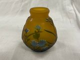 un vase jaune orné de fleurs bleues, posé sur une nappe blanche