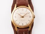 une montre en or avec un bracelet en cuir marron sur un fond blanc