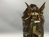 statue en bronze représentant une femme ailée posée sur un rocher, avec des nuages en arrière-plan