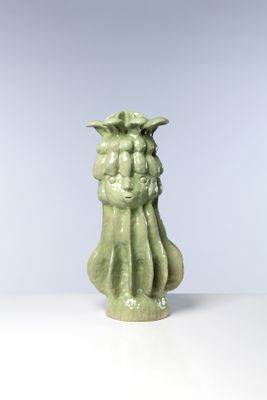 un vase vert orné d'un visage, posé sur une table