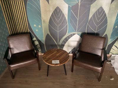 two chairs and a table in front of a wall with leaves