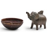 une statue d'éléphant à côté d'un bol, posée sur une surface blanche