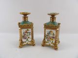 pair of gold and green vases with flowers on them on a white surface