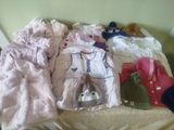 a pile of baby clothes on a bed next to a teddy bear