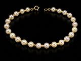 a gold bracelet with pearls on a black background