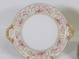 a white plate with pink flowers on it next to a stack of cups and saucers