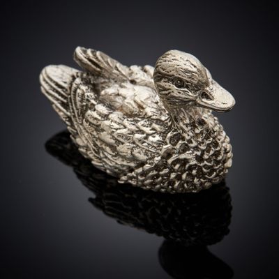 un gros plan d'une figurine de canard en argent posée sur une surface noire