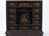 une vieille commode noire et dorée sur laquelle est posée une horloge