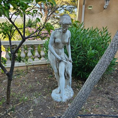 une statue représentant une femme assise sur un banc dans un jardin