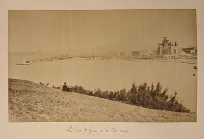 a black and white photo of a man sitting on a hill overlooking a body of water