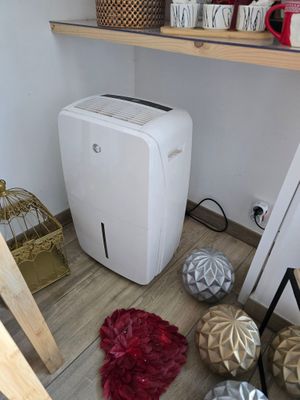 un petit climatiseur blanc posé par terre à côté d'une étagère