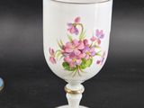 a white cup with purple flowers on it next to a blue and white plate
