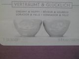 deux bols blancs ornés de visages, posés sur une table violette